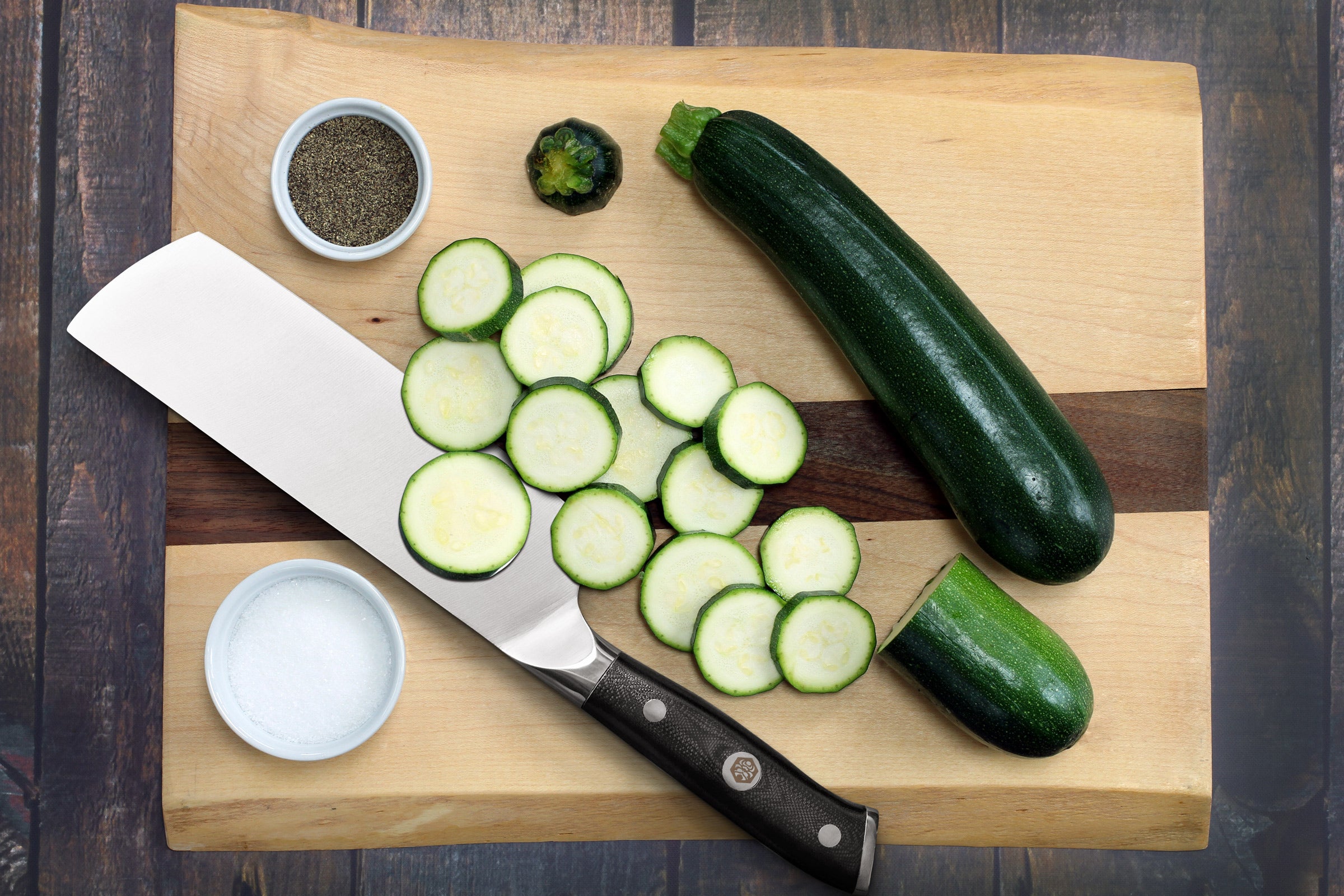 The Dynasty Nakiri on a cutting board with sliced zucchini, and small dishes of black pepper and sale.