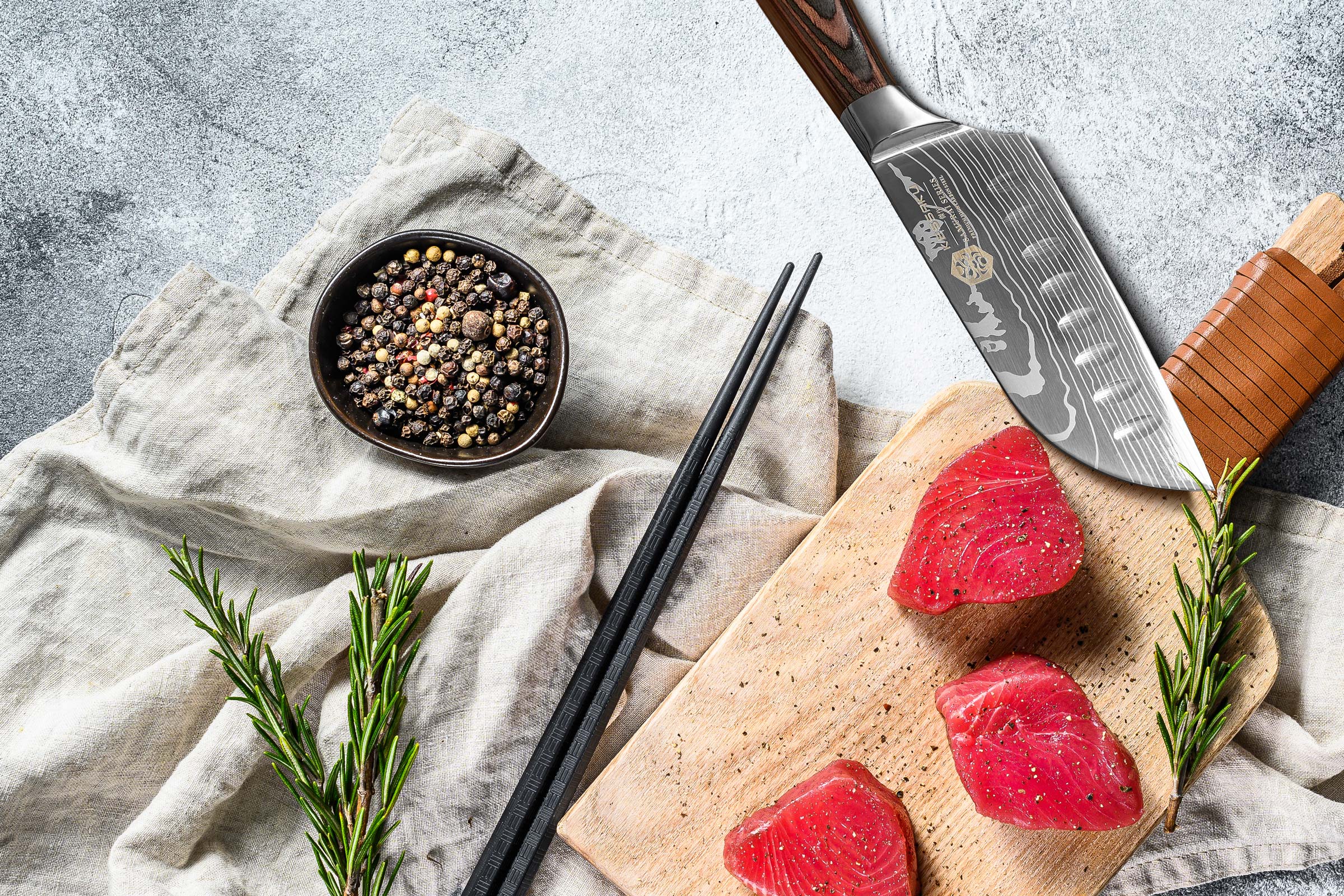 The Samurai 5" Santoku with chunks of red tuna sushi, black pepper, rosemary, and chopsticks