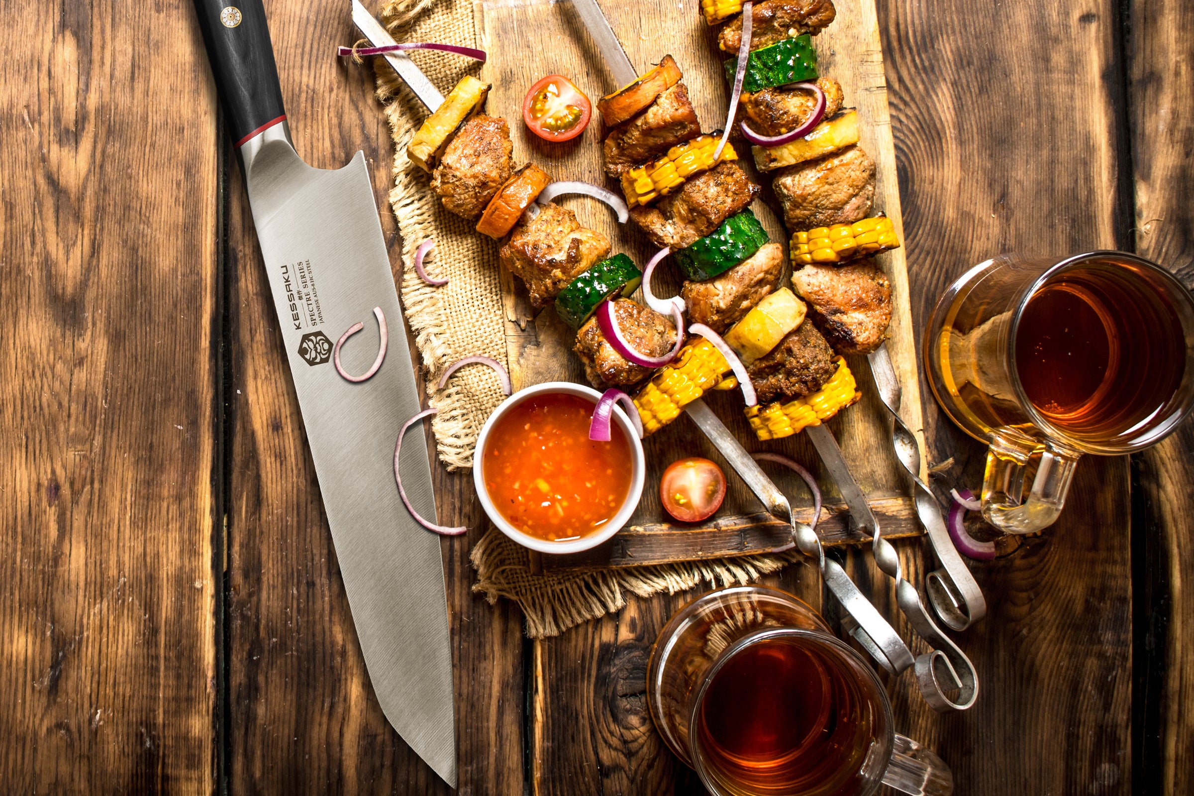 The Spectre K-Tip Chef's Knife next to skewers full of chicken, red onion, corn, squash, and cherry tomato