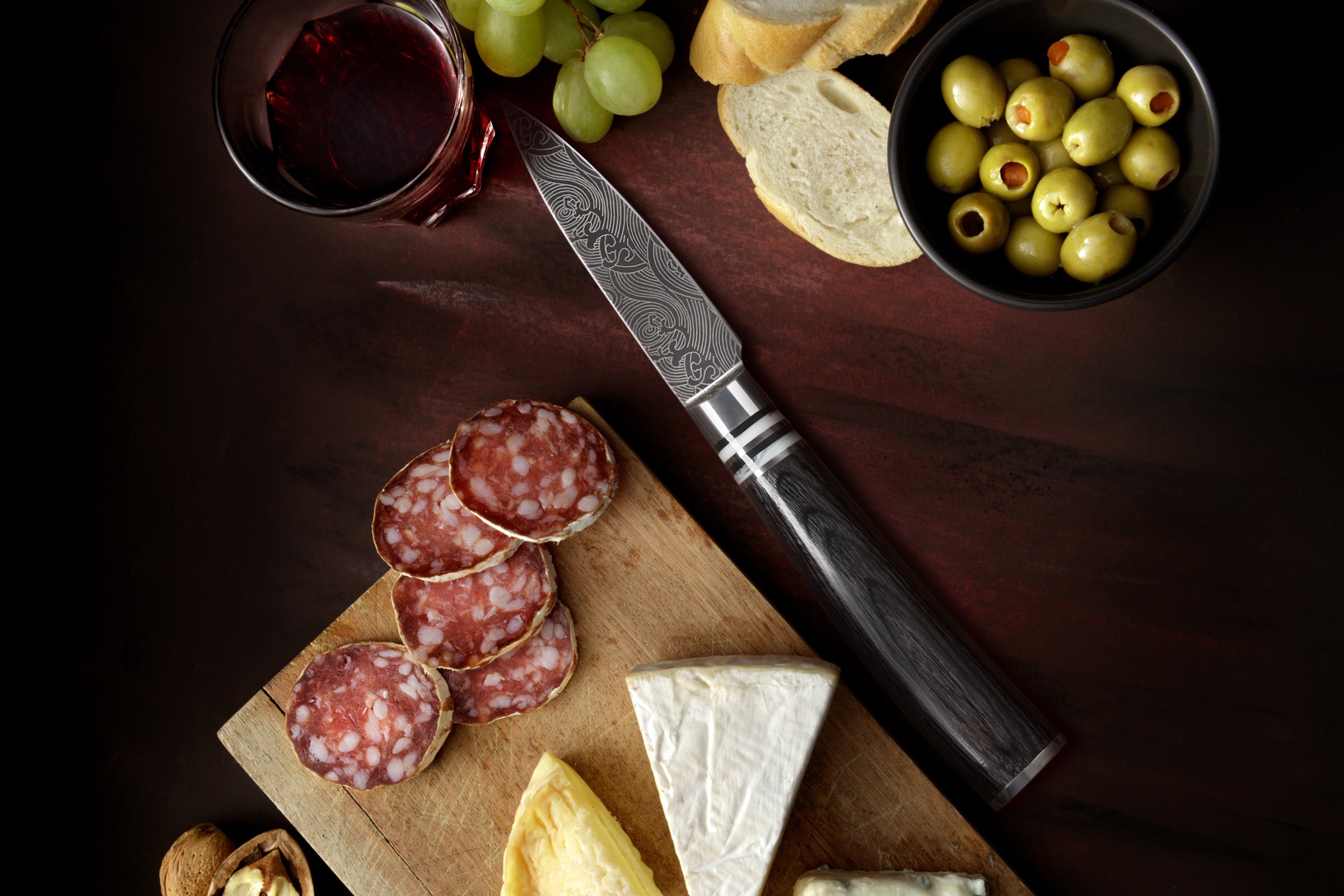 The Ronin Paring knife with slices of cured meat, bread, cheese, green grapes, and a glass of red wine.