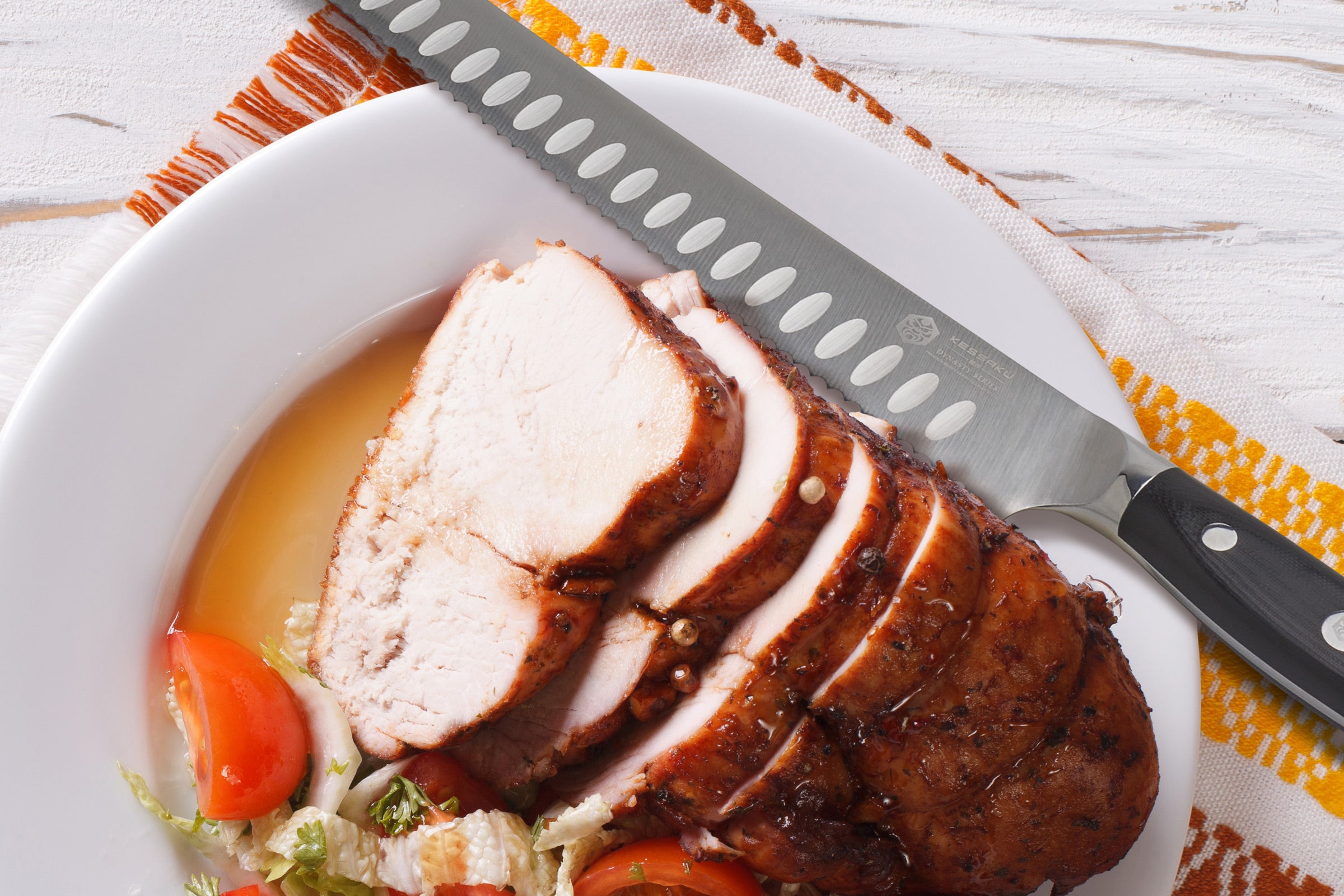 The Dynasty Serrated Carving Knife next to a plate of thick, sliced chicken.