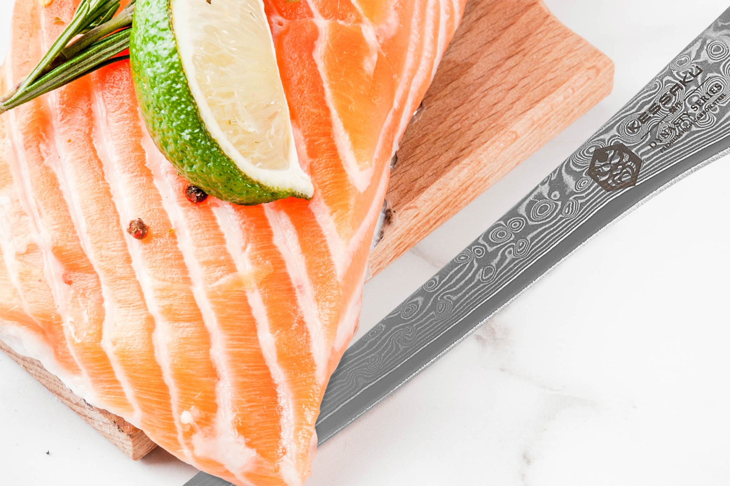 The Kessaku Dynasty Damascus Fillet Knife next to a salmon steak with a wedge of lime.